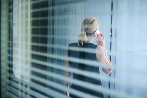 Eine Frau steht in einem Büror und telefoniert während die aus dem Fenster blickt