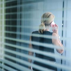 Eine Frau steht in einem Büror und telefoniert während die aus dem Fenster blickt