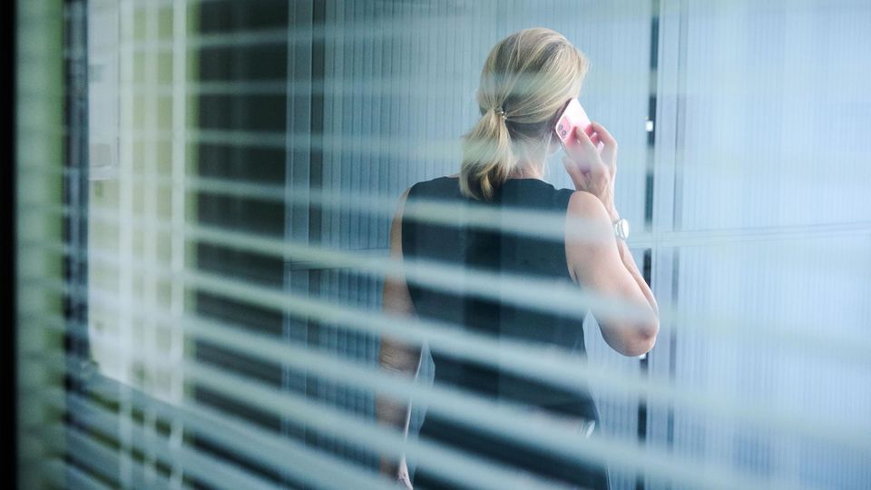 Falsche Stelle, kein Arbeitslosengeld: So funktioniert "Job-Scamming" Eine Frau steht in einem Büror und telefoniert während die aus dem Fenster blickt