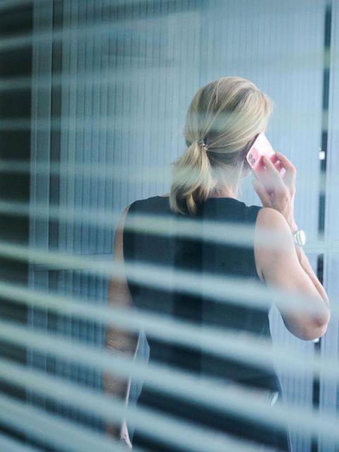 Eine Frau steht in einem Büror und telefoniert während die aus dem Fenster blickt