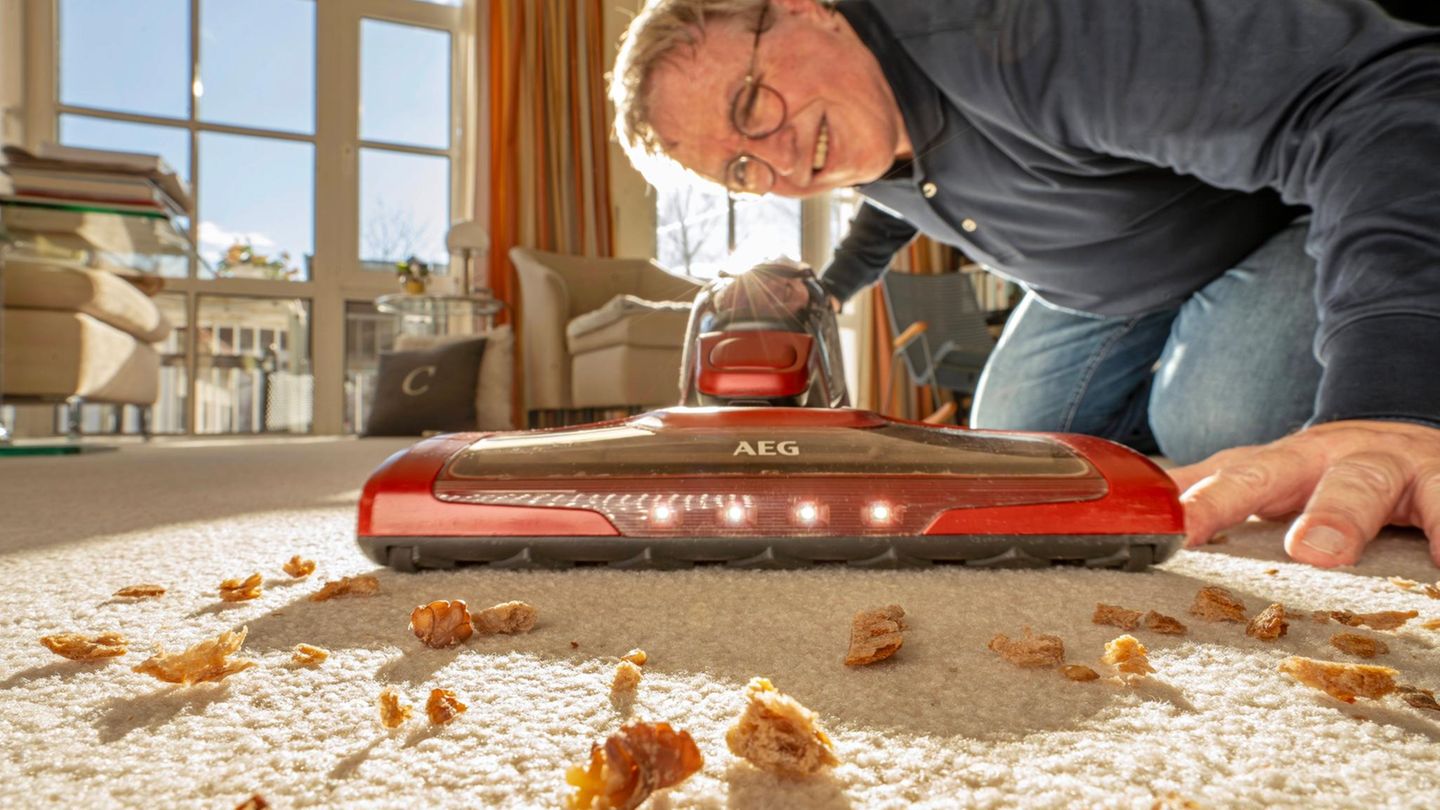 Ein Mann saugt mit einem Akku-Staubsauger den Teppich