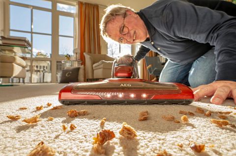 Ein Mann saugt mit einem Akku-Staubsauger den Teppich