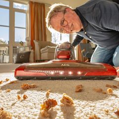 Ein Mann saugt mit einem Akku-Staubsauger den Teppich