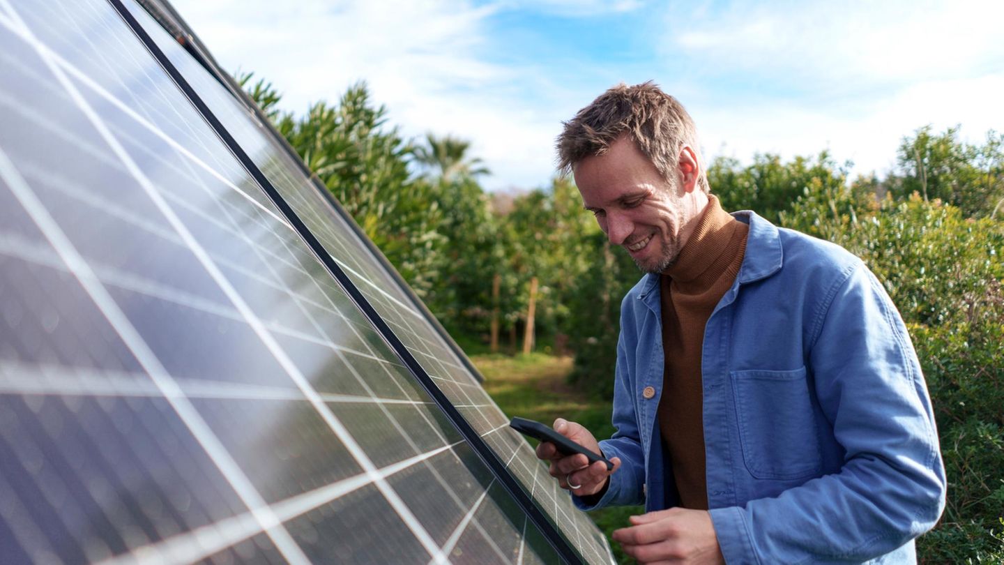 Solarmodule-Varianten Ein Manns steht neben einem Solarpanel und blickt auf sein Smartphone