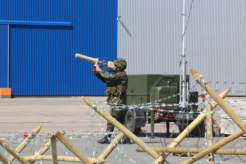 Ein maskierter Bundeswehrsoldat zielt mit eine Art Strahlenkanone auf eine rote Drohne, die vor ihm fliegt