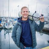 Der Forschungstaucher Florian Huber steht mit einer Druckluftflasche auf der Schulter in einen Yachthafen