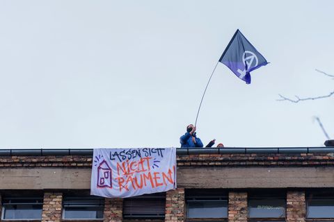 Ein Aktivist steht mit einer Fahne auf dem Dach der Dondorf-Druckerei mit einem Banner „Lassen sich nicht Räumen“. (Archivbild)