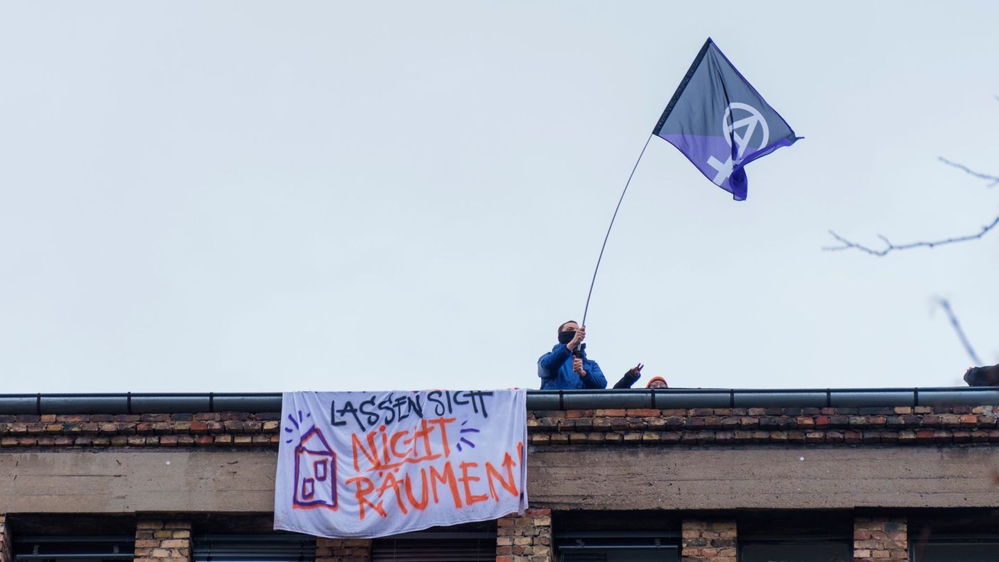 Ein Aktivist steht mit einer Fahne auf dem Dach der Dondorf-Druckerei mit einem Banner „Lassen sich nicht Räumen“. (Archivbild)