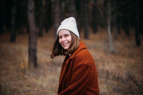Eine Frau steht im Wald. Sie lächelt in die Kamera.