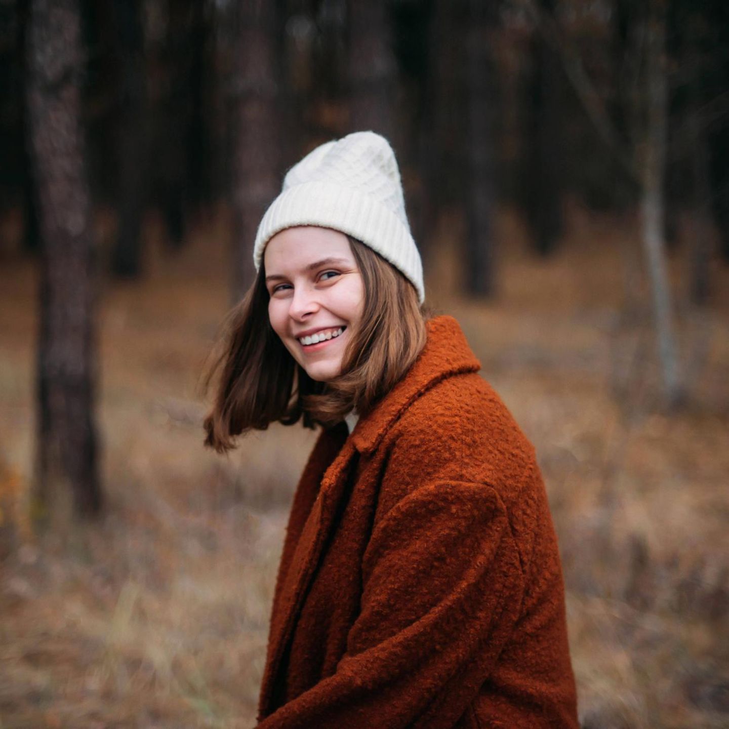 Eine Frau steht im Wald. Sie lächelt in die Kamera.