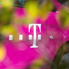 Magentafarbenes Fahrzeug der deutschen Telekom mit Firmenlogo hinter einer Hecke