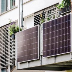 Zwei Solarpanels hängen an einer Balkonbrüstung, das Haus im Hintergrund ist hell verputzt.