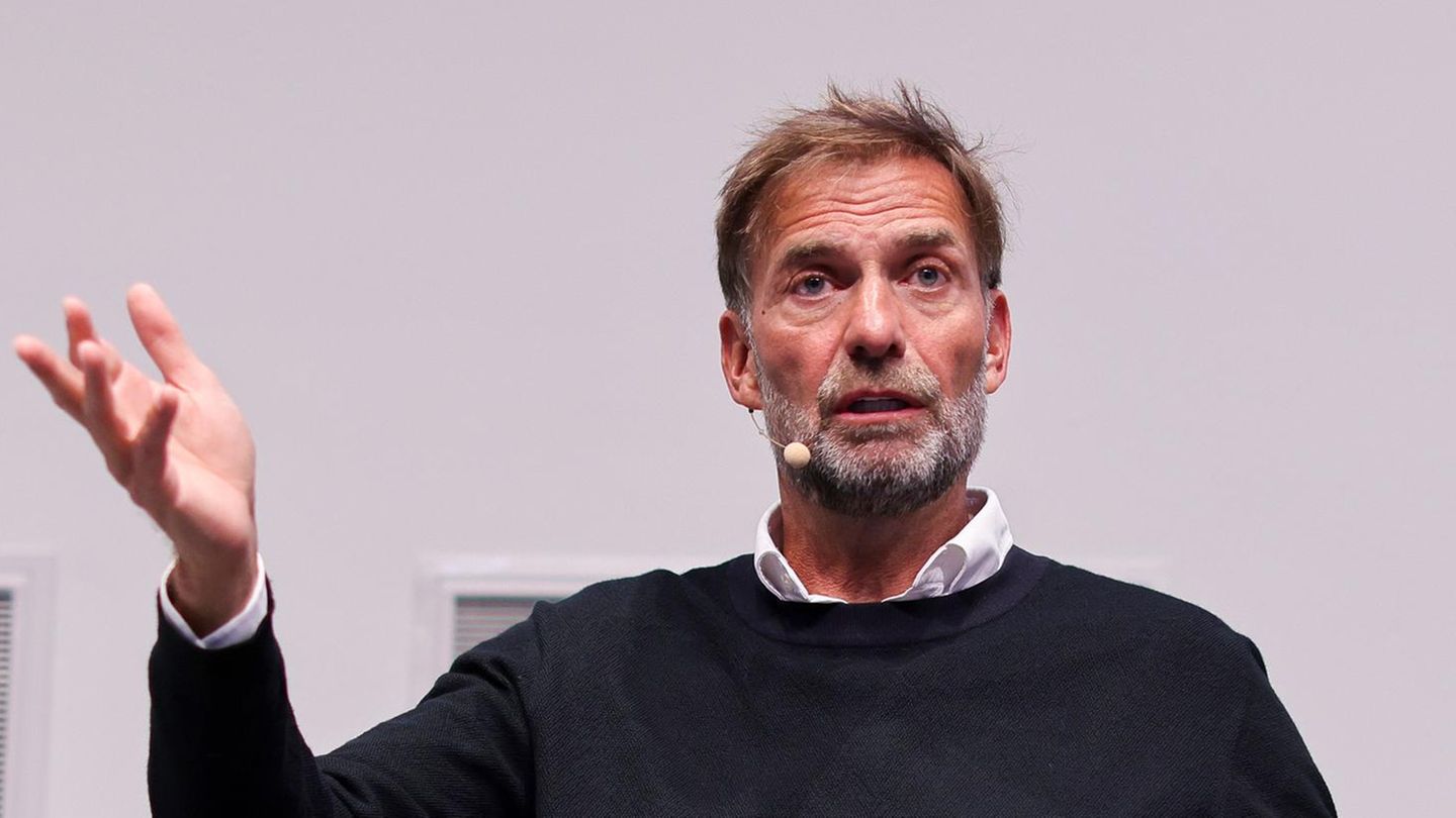 Jürgen Klopp sitzt auf einer Bühne und gestikuliert beim Sprechen mit erhobener rechter Hand