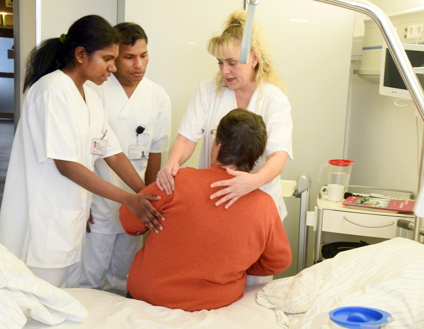 Eine Praxisanleiterin zeigt Auszubildenden in der Pflege den Umgang mit einer Patientin