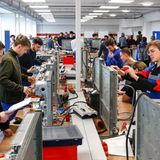 Gewerblich technisch Auszubildende stehen in einer Reihe und hantieren mit Kabeln