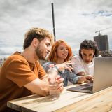 Studenten sitzen auf einer Dachterasse und schauen in einen Laptop