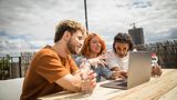 Studenten sitzen auf einer Dachterasse und schauen in einen Laptop