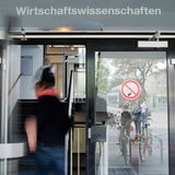 Studierende betreten eine Tür, über der Wirtschaftswissenschaften steht