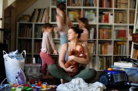 Muttersein Eine Mutter sitzt im Spielzimmer umringt von ihren Kindern Muttersein Eine Mutter sitzt im Spielzimmer umringt von ihren Kindern
