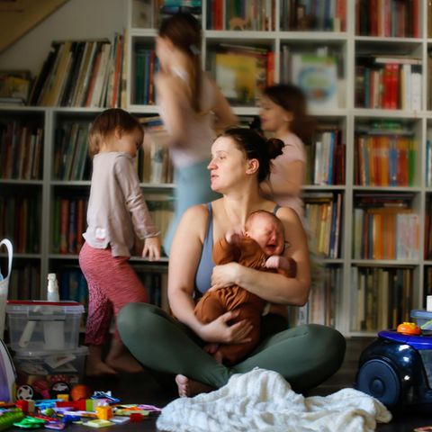 Muttersein Eine Mutter sitzt im Spielzimmer umringt von ihren Kindern Muttersein Eine Mutter sitzt im Spielzimmer umringt von ihren Kindern