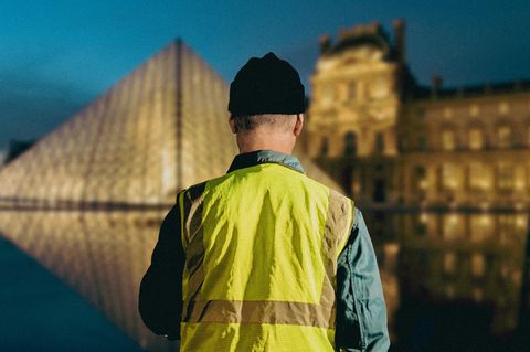 Ein Mann in Warnweste blickt auf den Louvre