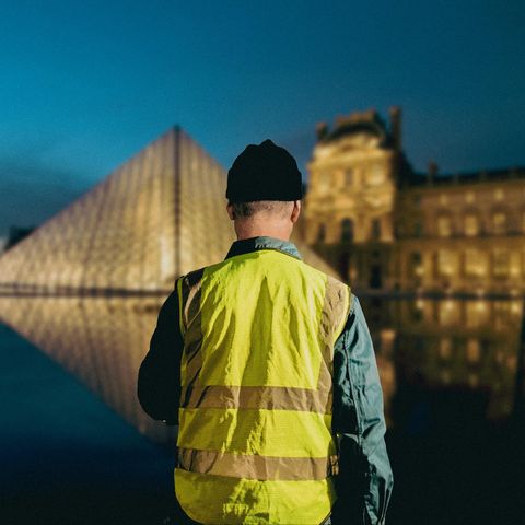 Ein Mann in Warnweste blickt auf den Louvre