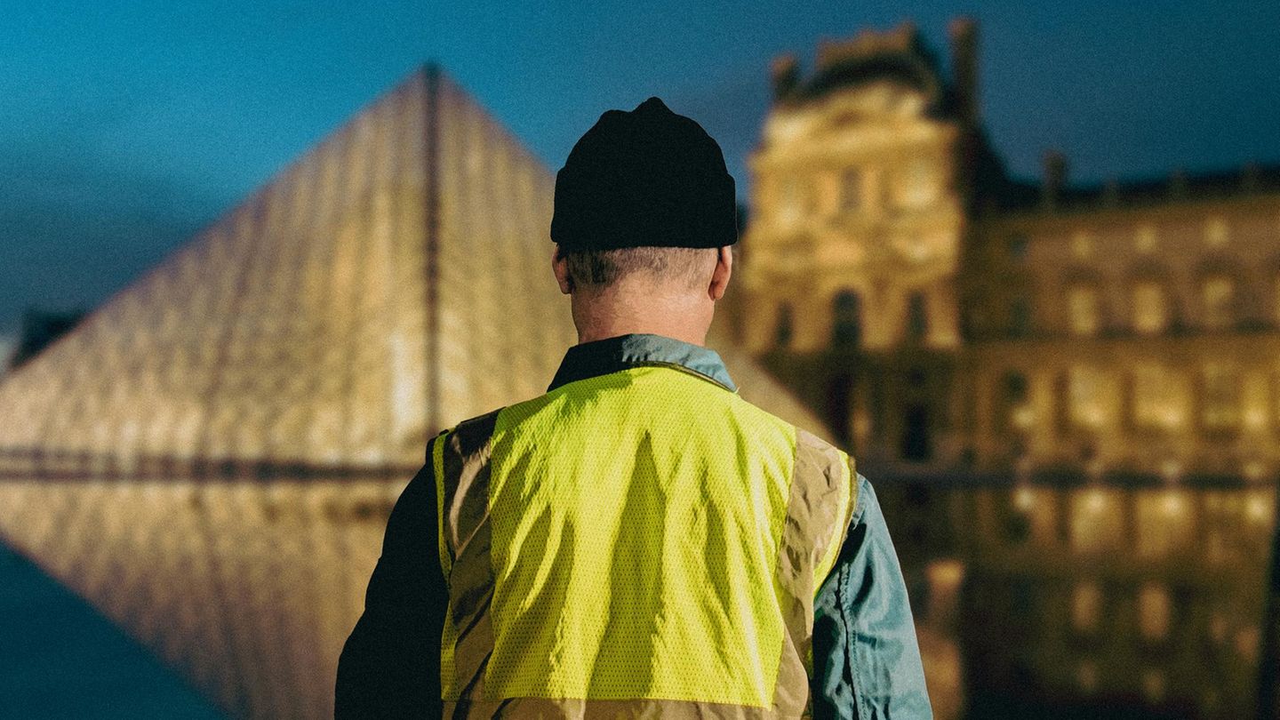 Ein Mann in Warnweste blickt auf den Louvre Ein Mann in Warnweste blickt auf den Louvre