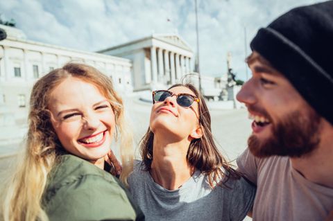 Polyamorie: Zwei Frauen und ein Mann lächeln sich im Arm  Polyamorie: Zwei Frauen und ein Mann lächeln sich im Arm
