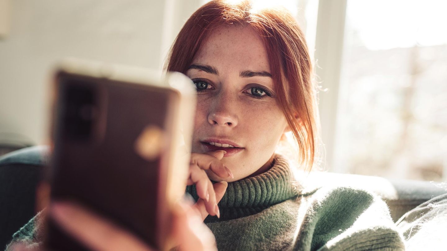 Eine junge Frau schaut auf ihr Smartphone und nutzt Whatsapp