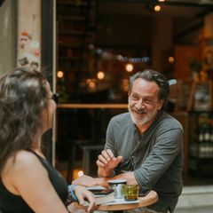 Ein älterer Mann sitzt an einem kleinen Tisch mit einer Frau im Cafe (Symbolbild Affäre).