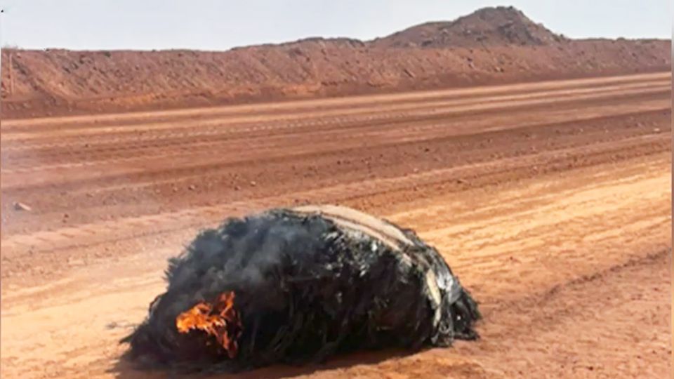 Verbrannter Metallklumpen: Experten vermuten: ein Teil aus dem Weltall. Experte in Schutzanzug begutachtet den großen Metallklumpen.