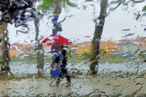 Eine Person geht mit aufgespanntem Schirm durch regnerisches Wetter