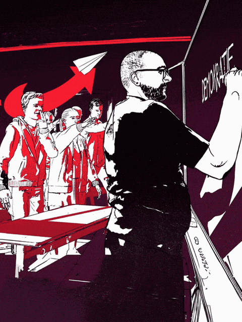 Der Lehrer schreibt "Demokratie" an die Tafel, während Schüler im Hintergrund den Hitlergruß zeigen