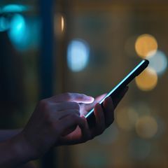 Eine Person schaut im Dunkeln auf ein leuchtendeds SMartphone und tippt SMS oder Whatsapp