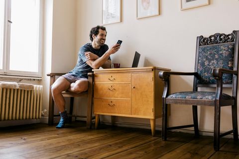 Ein Mann sitzt auf einem Stuhl und schaut lachend auf sein Smartphone