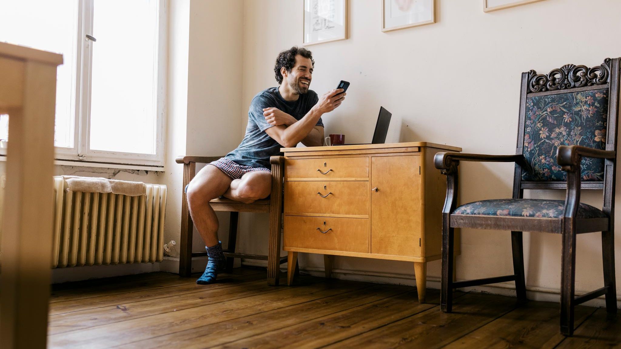 Ein Mann sitzt auf einem Stuhl und schaut lachend auf sein Smartphone