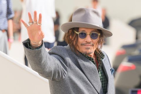 Johnny Depp winkt den Fotografen und trägt einen grauen Hut zum grauen Anzug