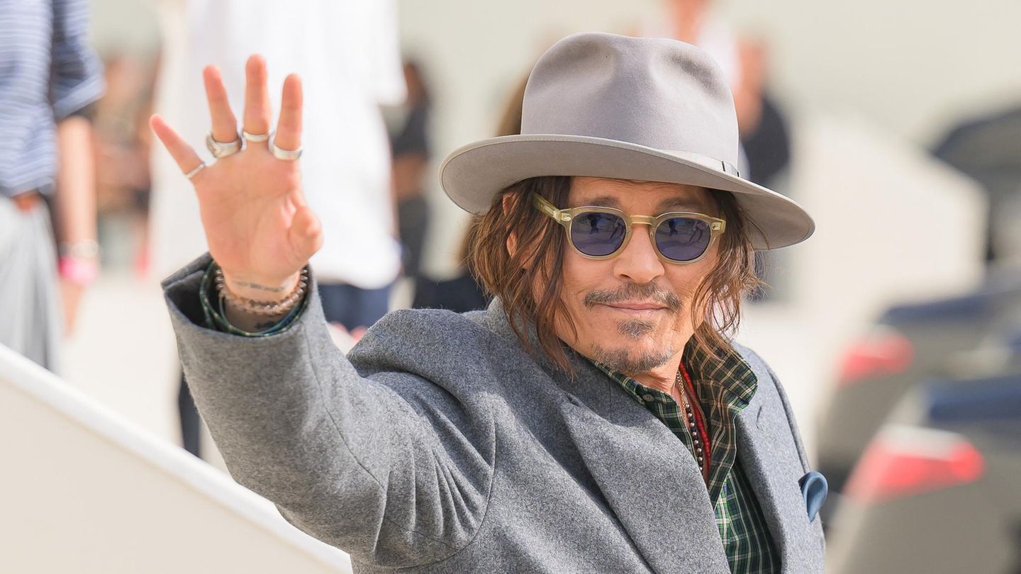 Johnny Depp winkt den Fotografen und trägt einen grauen Hut zum grauen Anzug