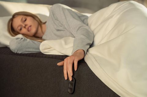 Eine Frau liegt auf der smarten Matratze Eight Sleep Pod und steuert sie mit Buttons an der Seite