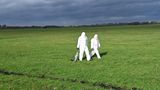 Menschen in weißen Schutzanzügen laufen über eine grüne Wiese