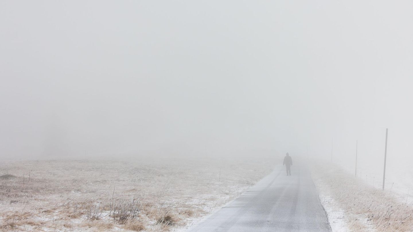 Zu sehen ist ein leicht verschneiter Weg mit einem Menschen in nebliger Landschaft