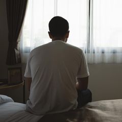 Junger Mann sitzt auf einer Bettkante