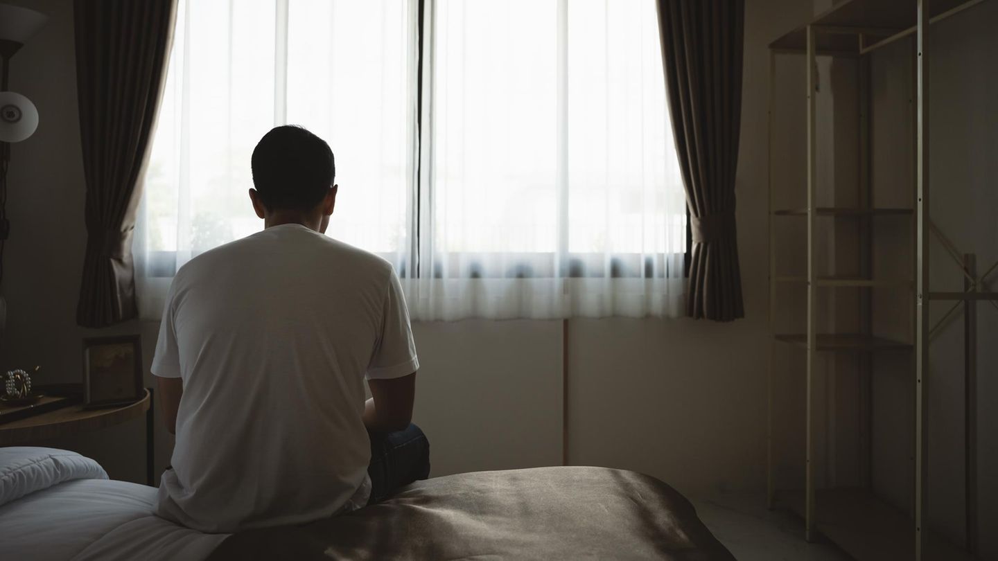 Junger Mann sitzt auf einer Bettkante