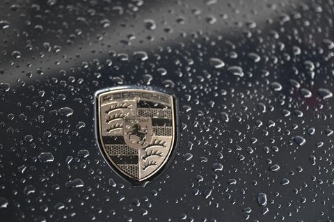 Das Logo von Porsche glänzt golden auf einer schwarzen Motorhaube voller Regentropfen