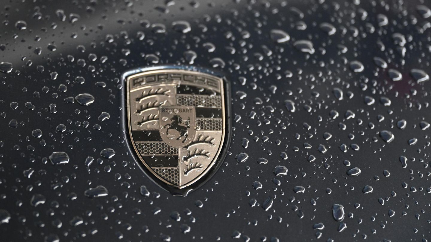 Porsche Das Logo von Porsche glänzt golden auf einer schwarzen Motorhaube voller Regentropfen