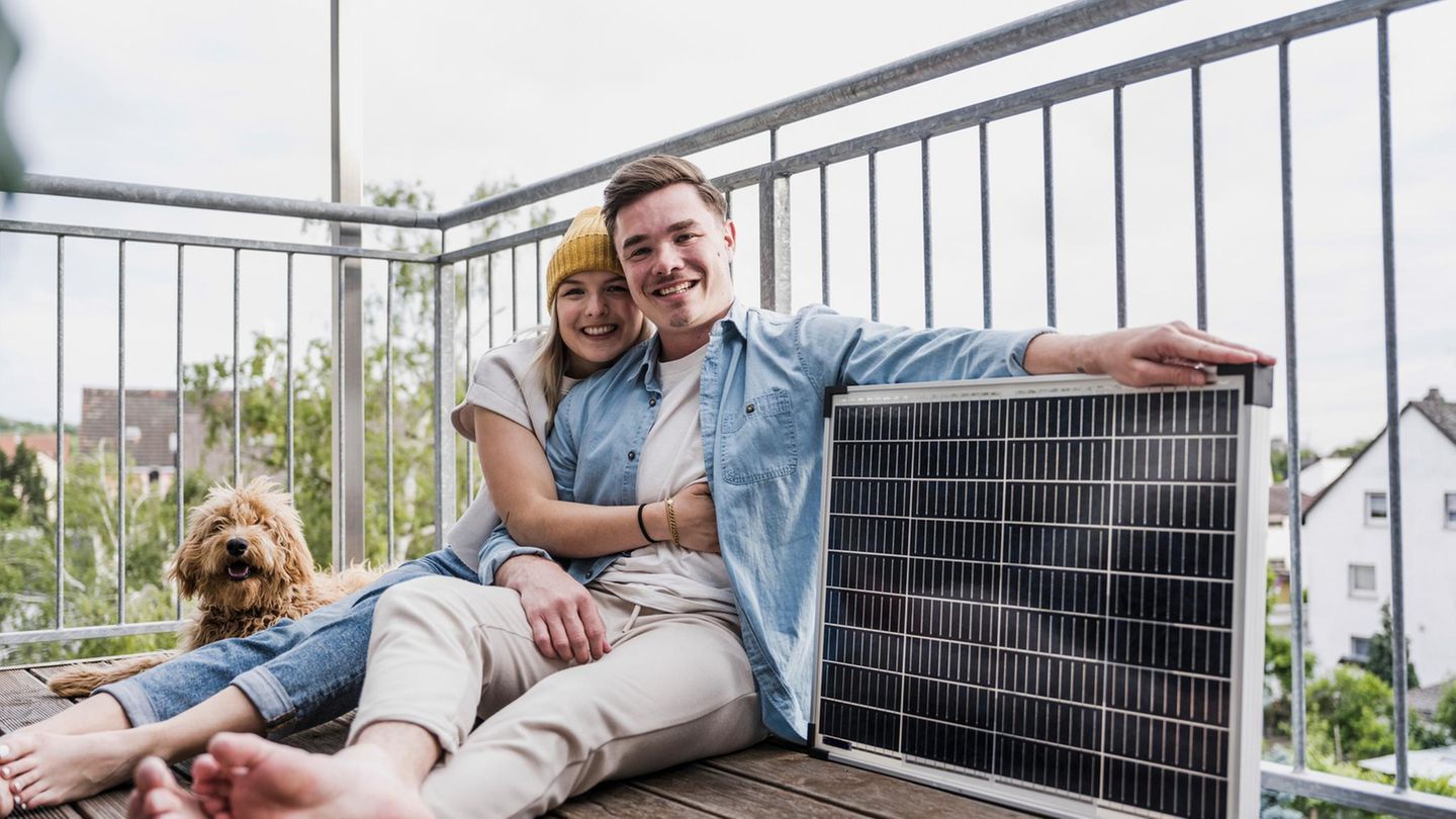 Zwei Menschen und ein Hund sitzen auf einem Balkon, der Mann hält das Solarpanel eines Balkonkraftwerkes