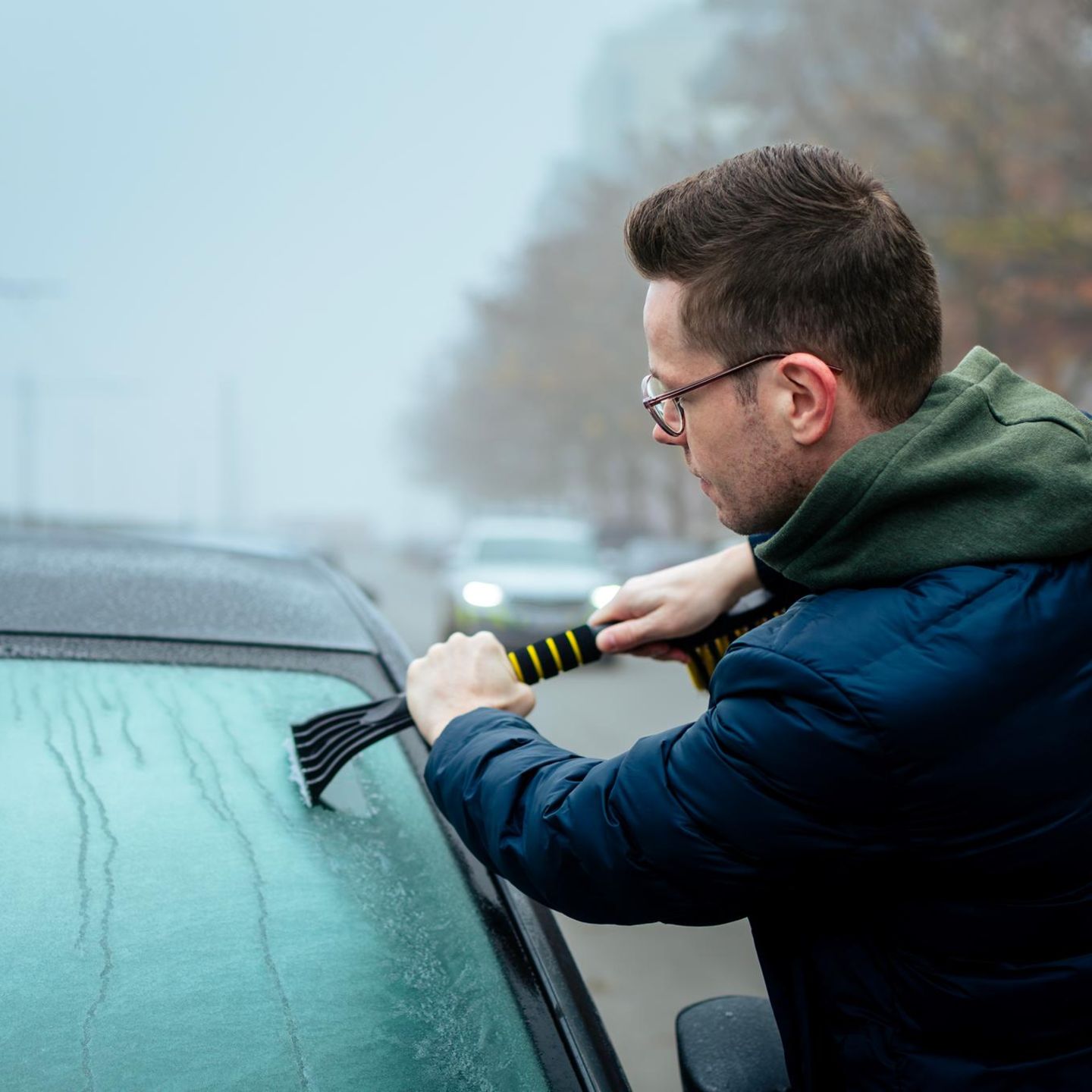 Man scraping snow off car windshield