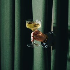 Eine Hand reicht ein Champagnerglas durch einen Vorhang Eine Hand reicht ein Champagnerglas durch einen Vorhang