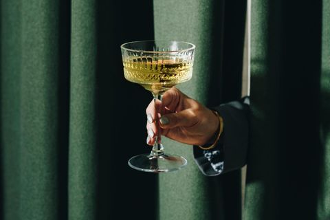 Eine Hand reicht ein Champagnerglas durch einen Vorhang Eine Hand reicht ein Champagnerglas durch einen Vorhang