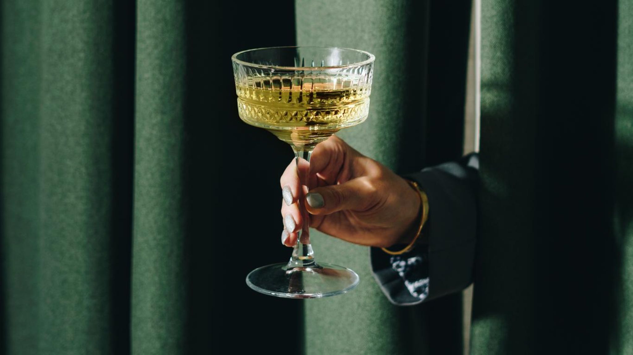 Eine Hand reicht ein Champagnerglas durch einen Vorhang Eine Hand reicht ein Champagnerglas durch einen Vorhang